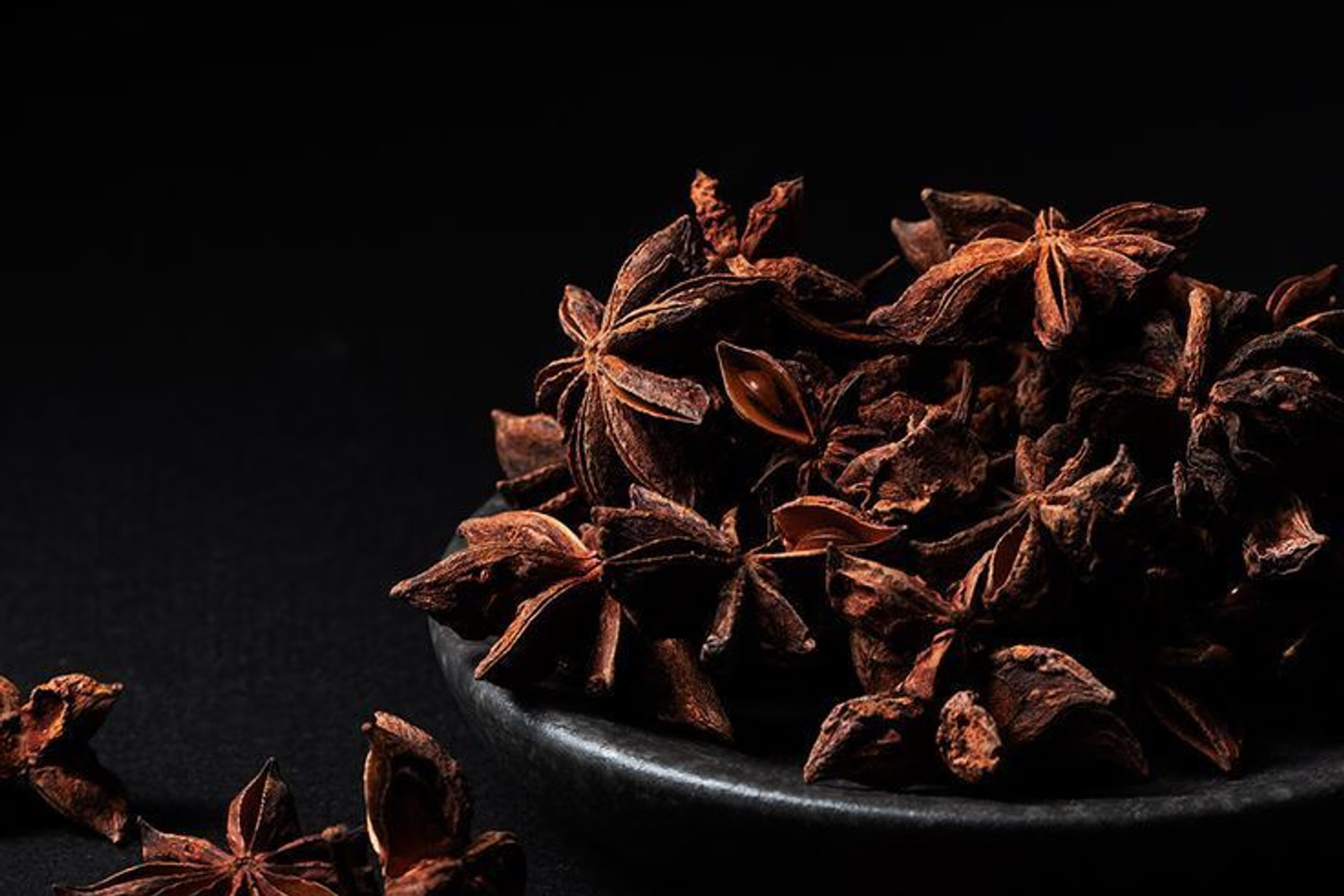 Dark chiaroscuro still life of whole spices on textured dark surface